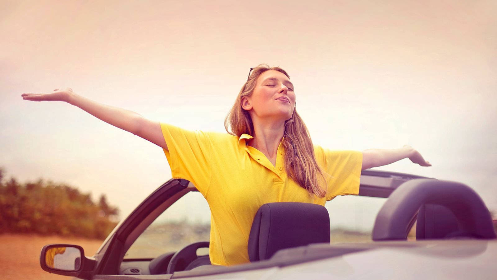 Vrouw die met haar armen in de lucht uit de cabrio komt