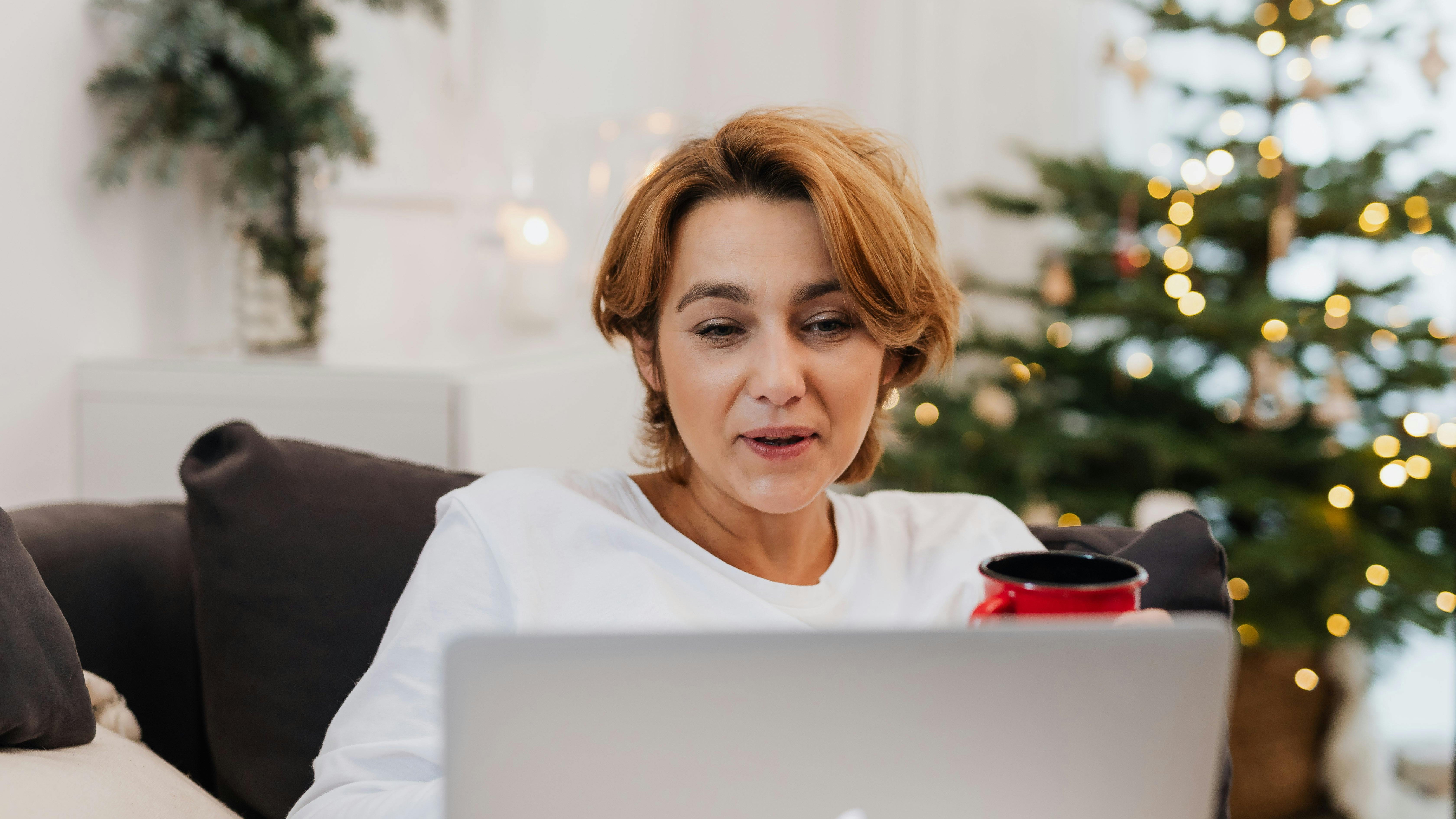 Vrouw achter haar laptop met een kerstboom op de achtergrond.